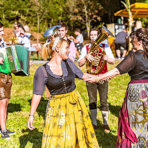 2 Frauen tanzen in Tracht mit Musikern im Hintergrund