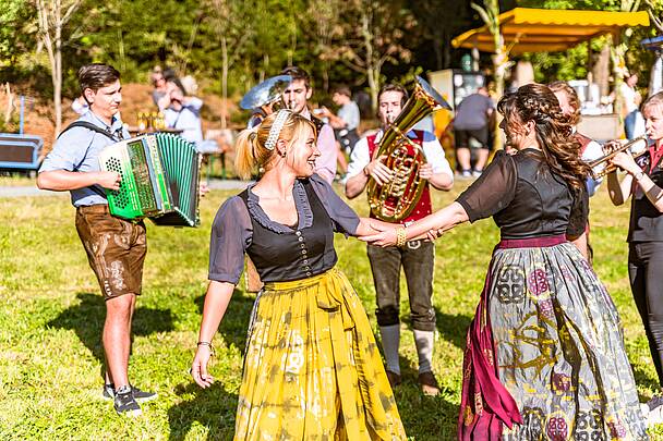 2 Frauen tanzen in Tracht mit Musikern im Hintergrund