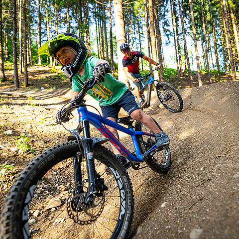 Kind fährt mit Helm in Skillscenter der Bike Area Obermillstatt und Vater fährt hinterher