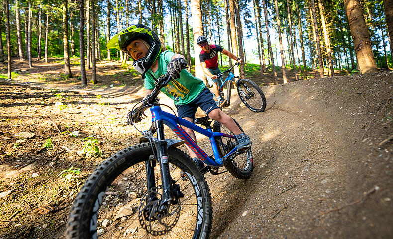 Kind fährt mit Helm in Skillscenter der Bike Area Obermillstatt und Vater fährt hinterher