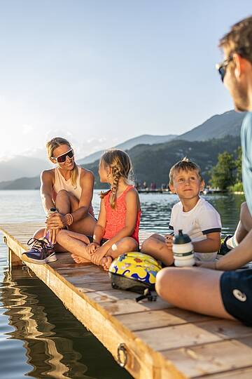 Familie sitzt im Herbst auf Steg am Millstätter See und genießt die Sonne