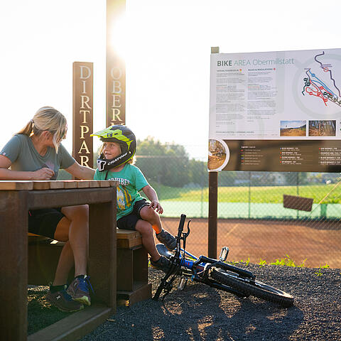 Mutter macht mit Kind Pause vom mountainbiken an einem Tisch in der Bike Area Obermillstatt