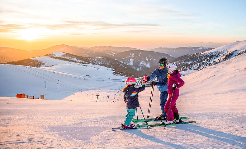 Familie steht mit Ski auf Piste am Falkert