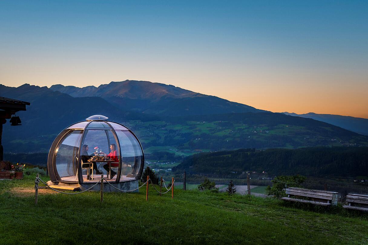 2 Personen genießen ihr Dinner in der Glaskuppel in einer Sommernacht